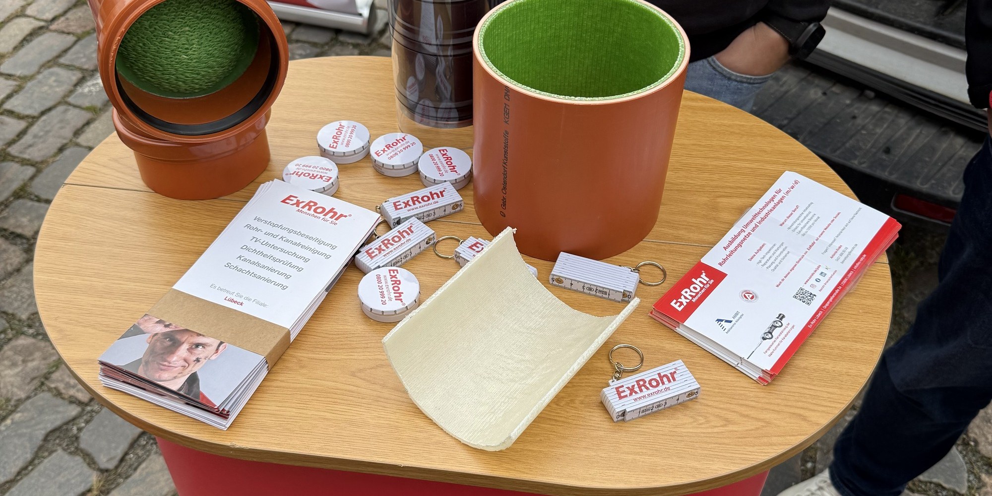 Stehtisch beim Messestand mit Rohrst&uuml;cken, im Anschnitt ein oranges Rohr mit gr&uuml;nem Inliner, dazu eine Gewebeprobe und Informationsmaterial