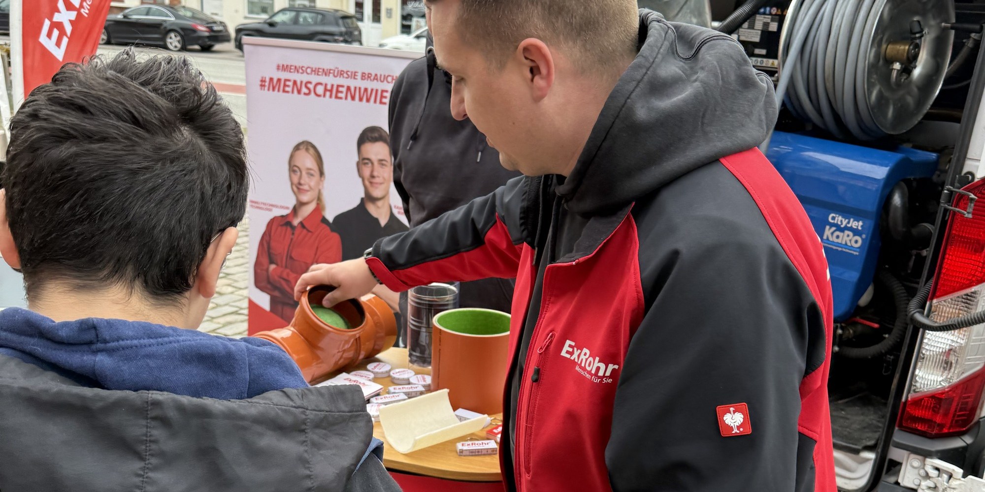 Mitarbeiter von ExRohr erkl&auml;rt einem Jugendlichen am Messestand ein Rohrst&uuml;ck, im Hintergrund die Schlauchhaspel im Fahrzeug