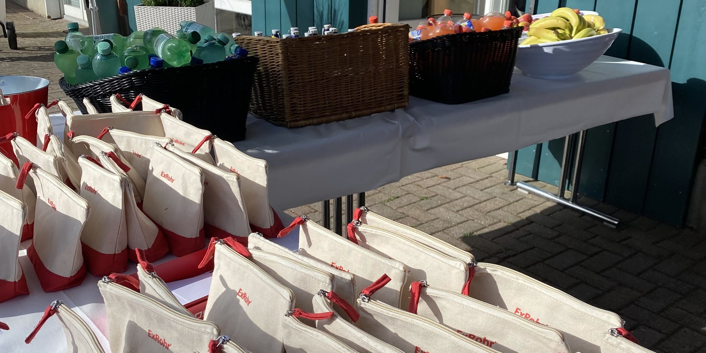 Aufgereihte Stofftaschen mit ExRohr-Logo und rotem Reissverschluss auf dem Empfangstisch beim Golfturnier