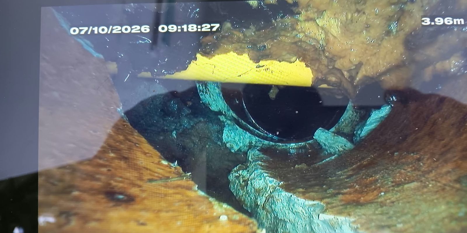Kamerabild aus einer Abwasserleitung, quer durch das Rohr verläuft ein gelbes Gasrohr