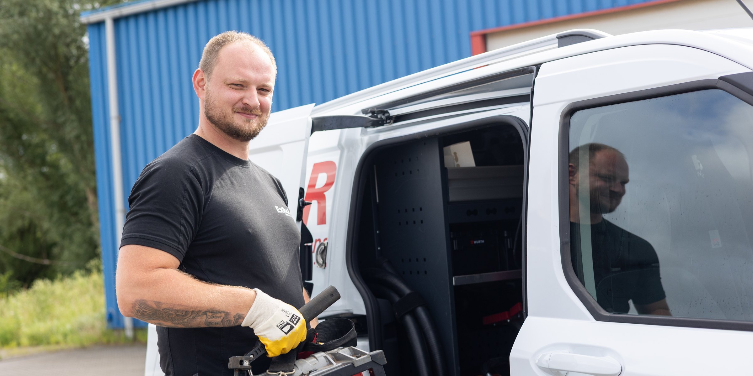 Monteur von ExRohr mit Arbeitshandschuhen und Inspektionsgerät am geöffneten Firmentransporter